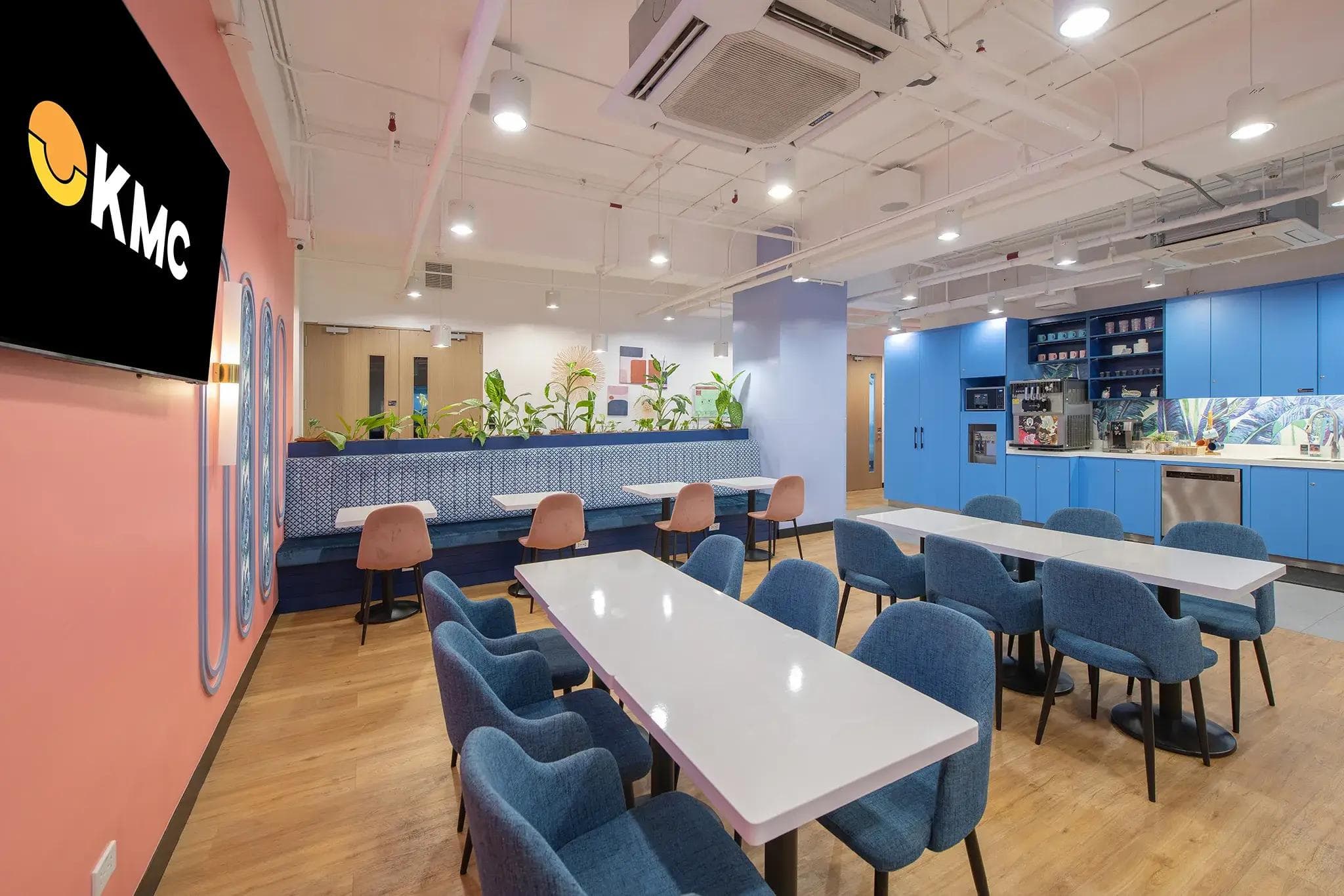 A modern office space in Lexmark, Cebu with blue chairs, pink walls, wood flooring, modern kitchen, and indoor plants.