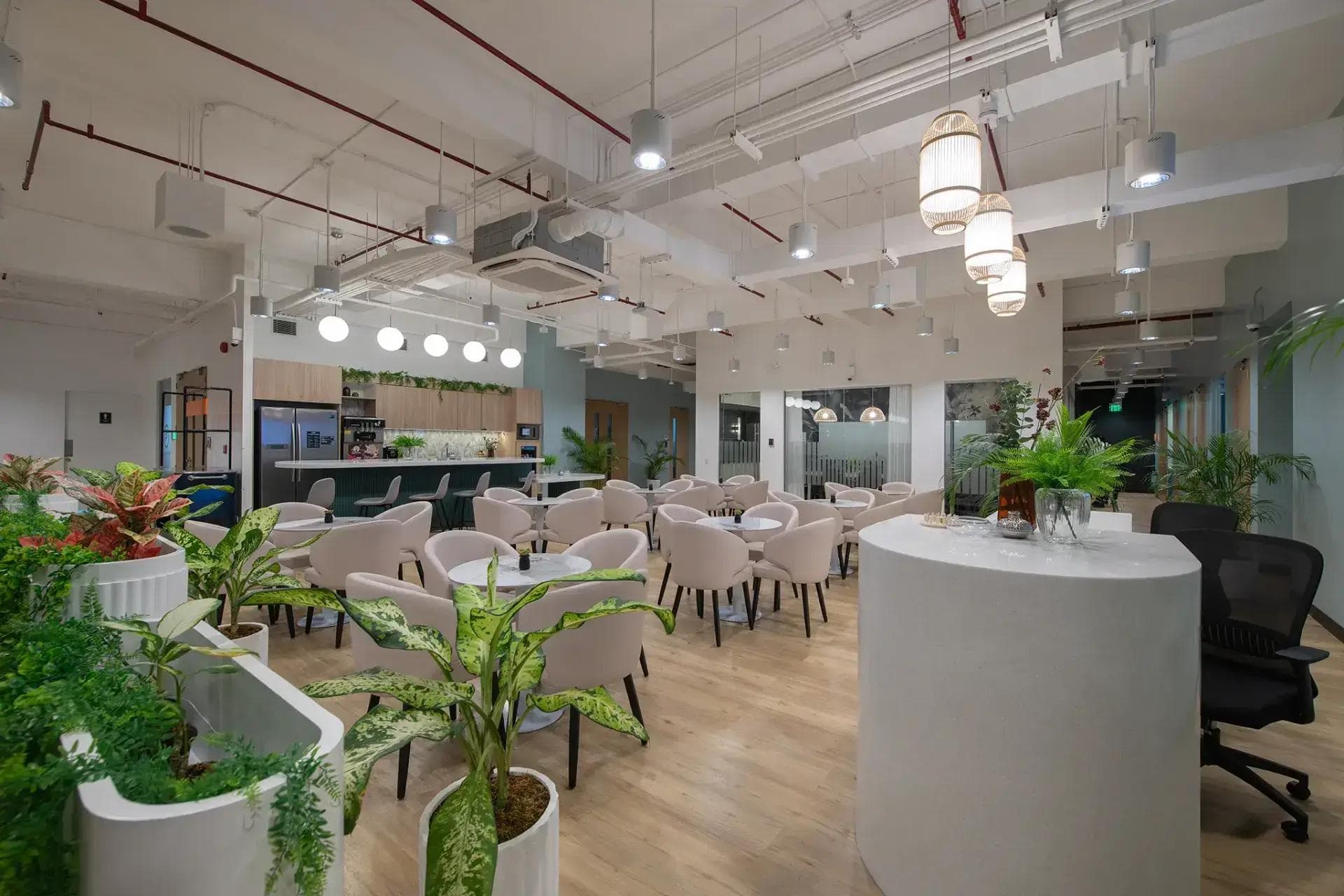 Skyrise 4A pantry area featuring pastel chairs, round tables, indoor plants, hanging lights, and a modern kitchen bar setup.