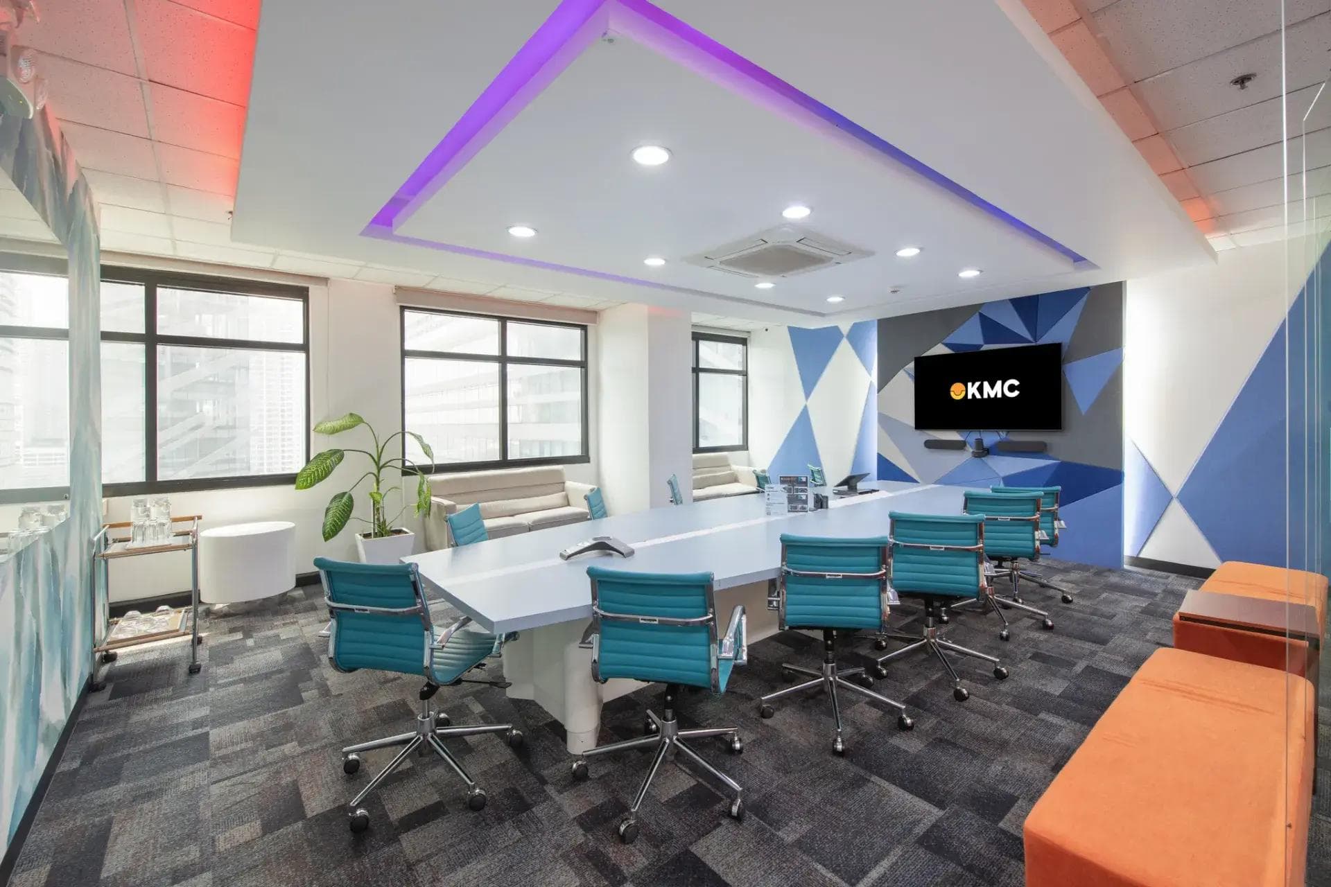 A vibrant meeting room in a BGC office space with geometric walls, blue chairs, LED ceiling lights, and a wall-mounted TV.
