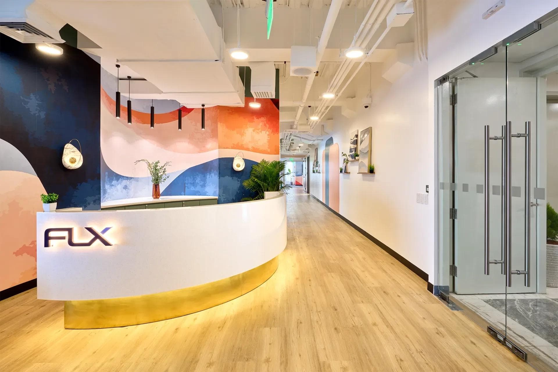 Modern FLX, Makati office space reception with curved desk, wood floors, abstract mural, and glass door entry.
