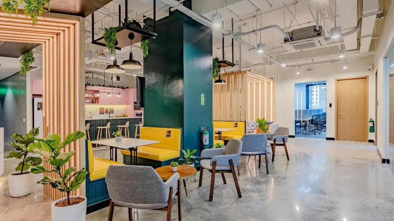 A vibrant workspace in Armstrong, Makati with modern furniture, yellow booth seats, lush greenery, and a stylish café bar.