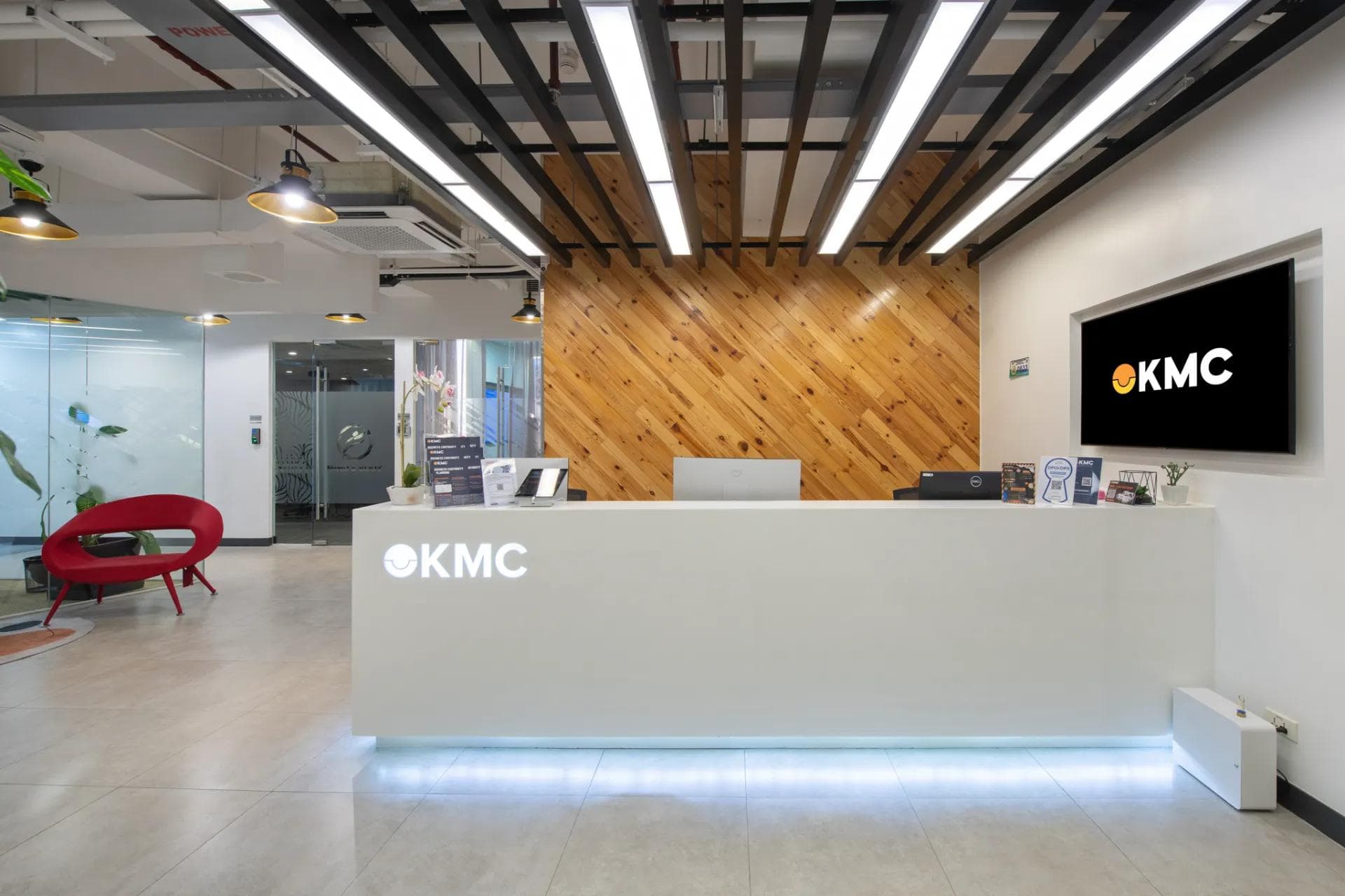 Reception area at KMC Rockwell Sheridan with a wood-accent wall, modern lighting, and a glowing, embossed front desk logo.