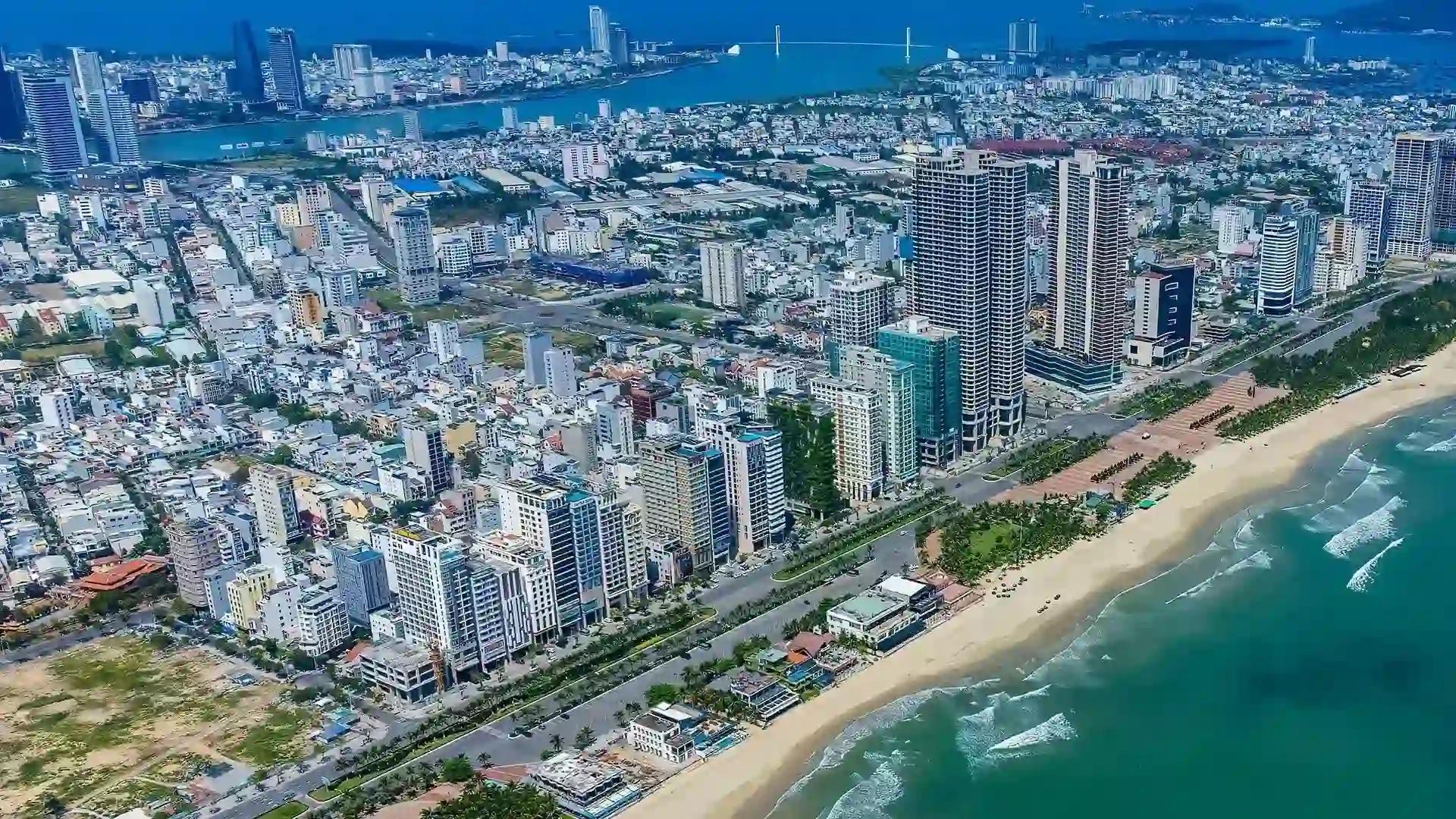 A vibrant coastal cityscape of Vietnam with high-rise buildings lining a scenic beach, overlooking calm blue waters.