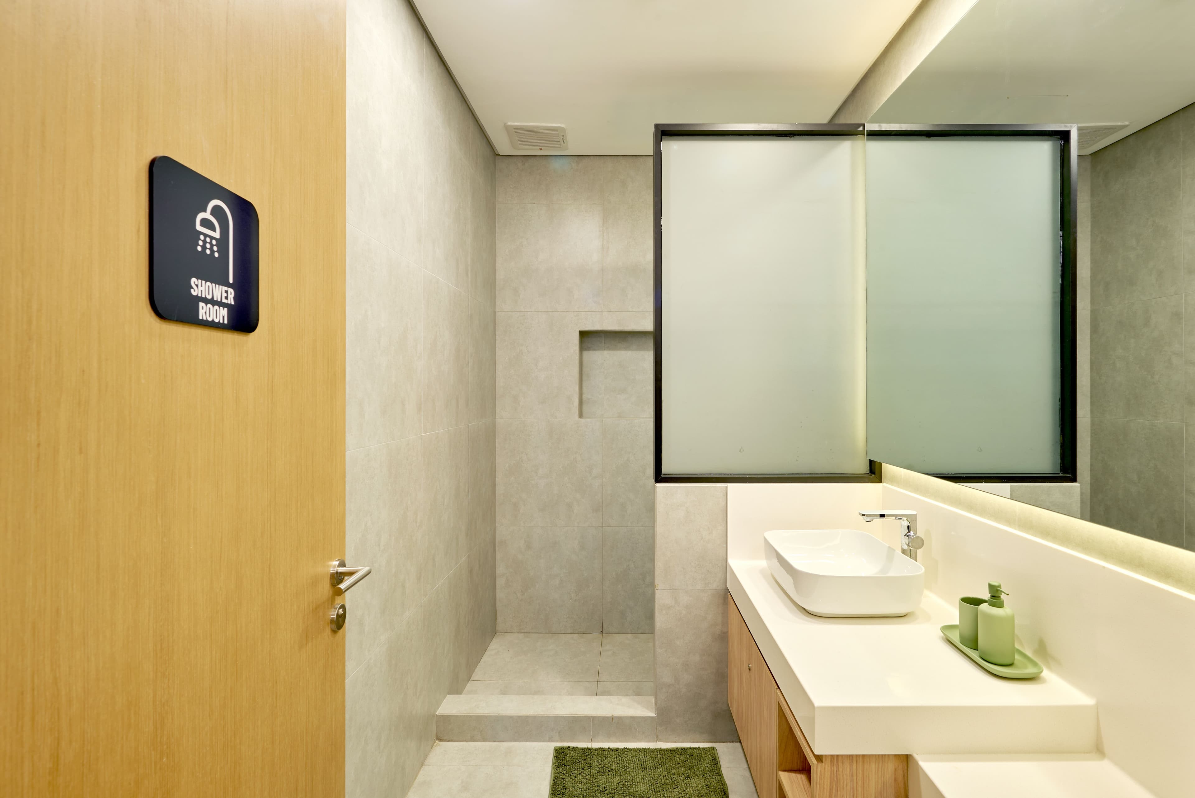 Modern restroom with gray marble walls, a sleek vanity with mirror and lights, woven baskets, and a black rainfall shower.