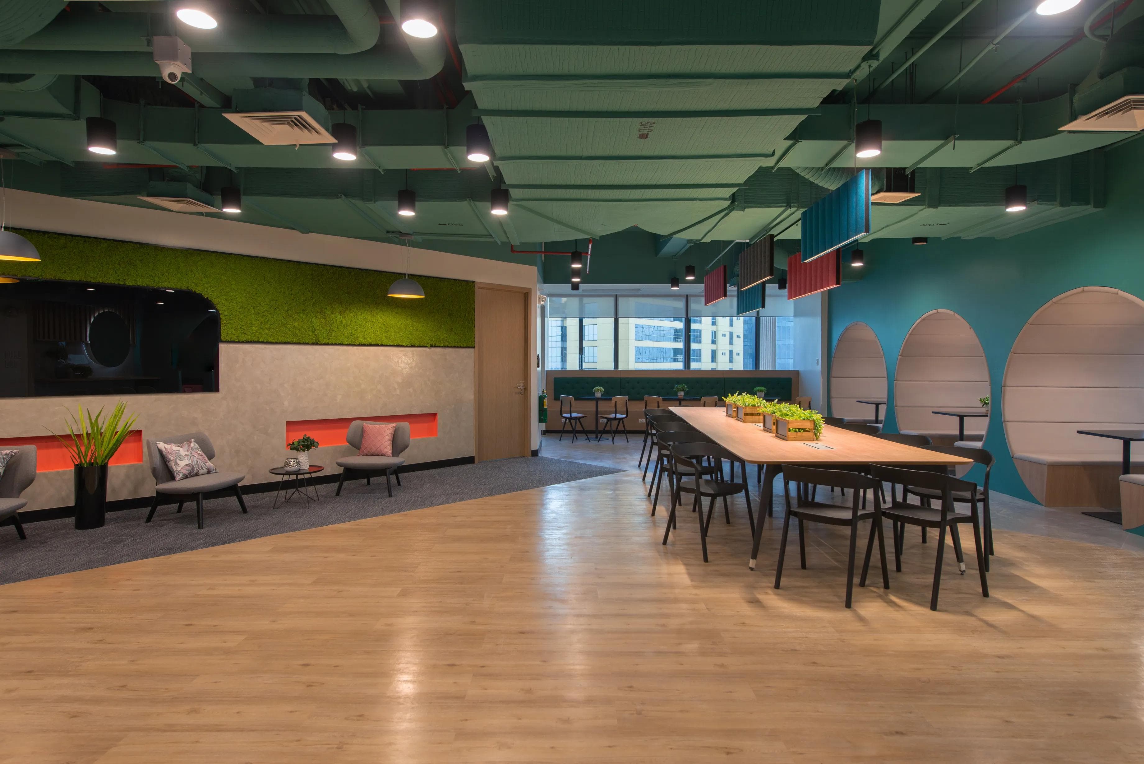 Modern coworking office with lush green walls, long table, 6 chairs, lounge seating, and window views for collaborative work.