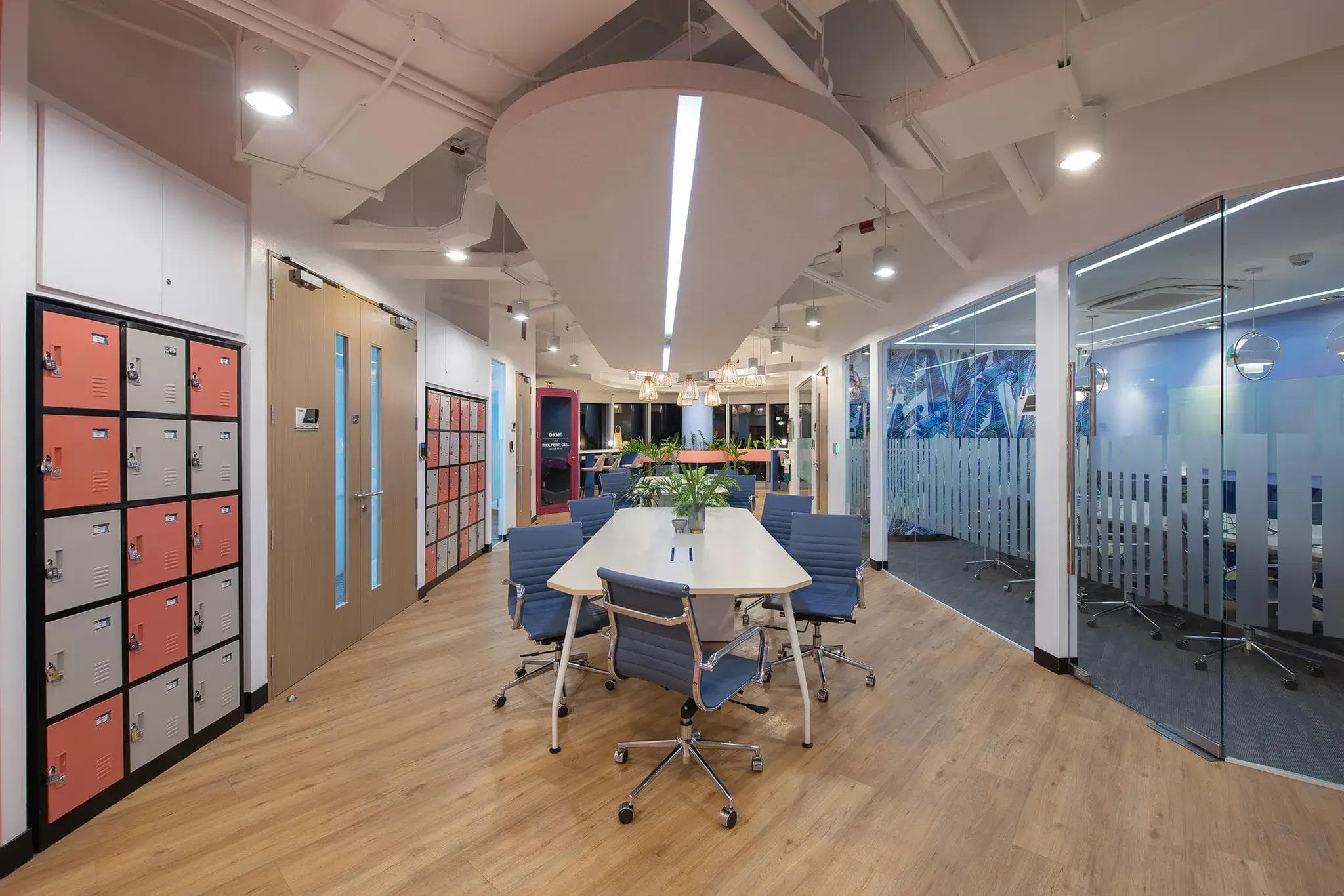 Modern office space in Cebu with wood flooring, blue chairs, glass-walled meeting rooms, lockers, hanging lights, and plants.