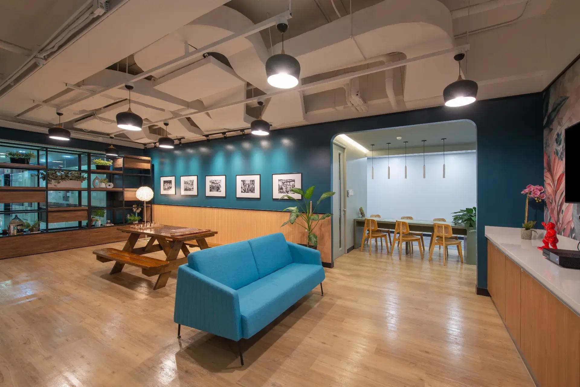 A cozy office lounge at Cybersigma, BGC - with a blue sofa, wooden table, framed photos, lush decor and warm lighting.