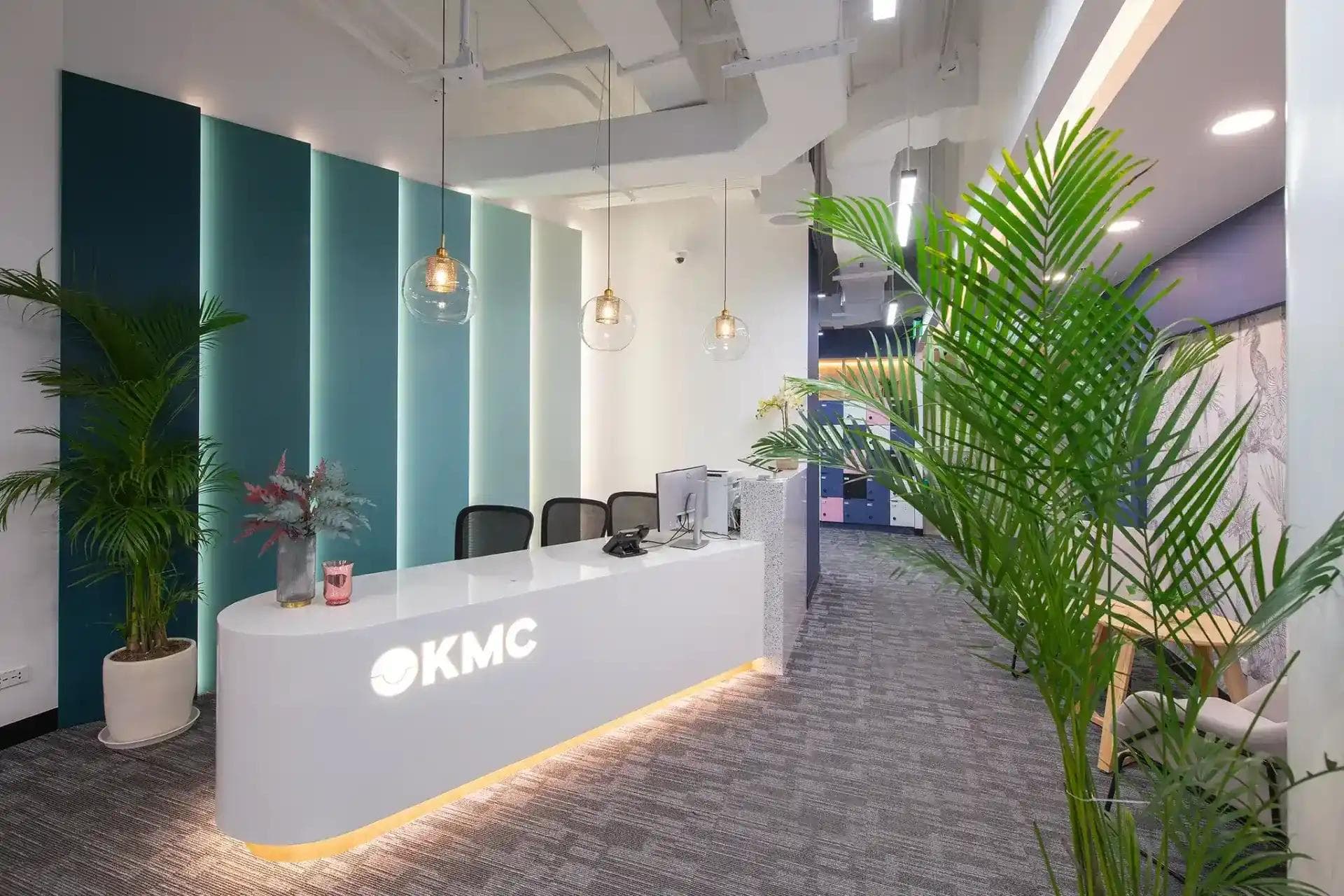 A sleek and modern reception area with an embossed KMC logo, ambient lighting, lush greenery, and stylish decorations.