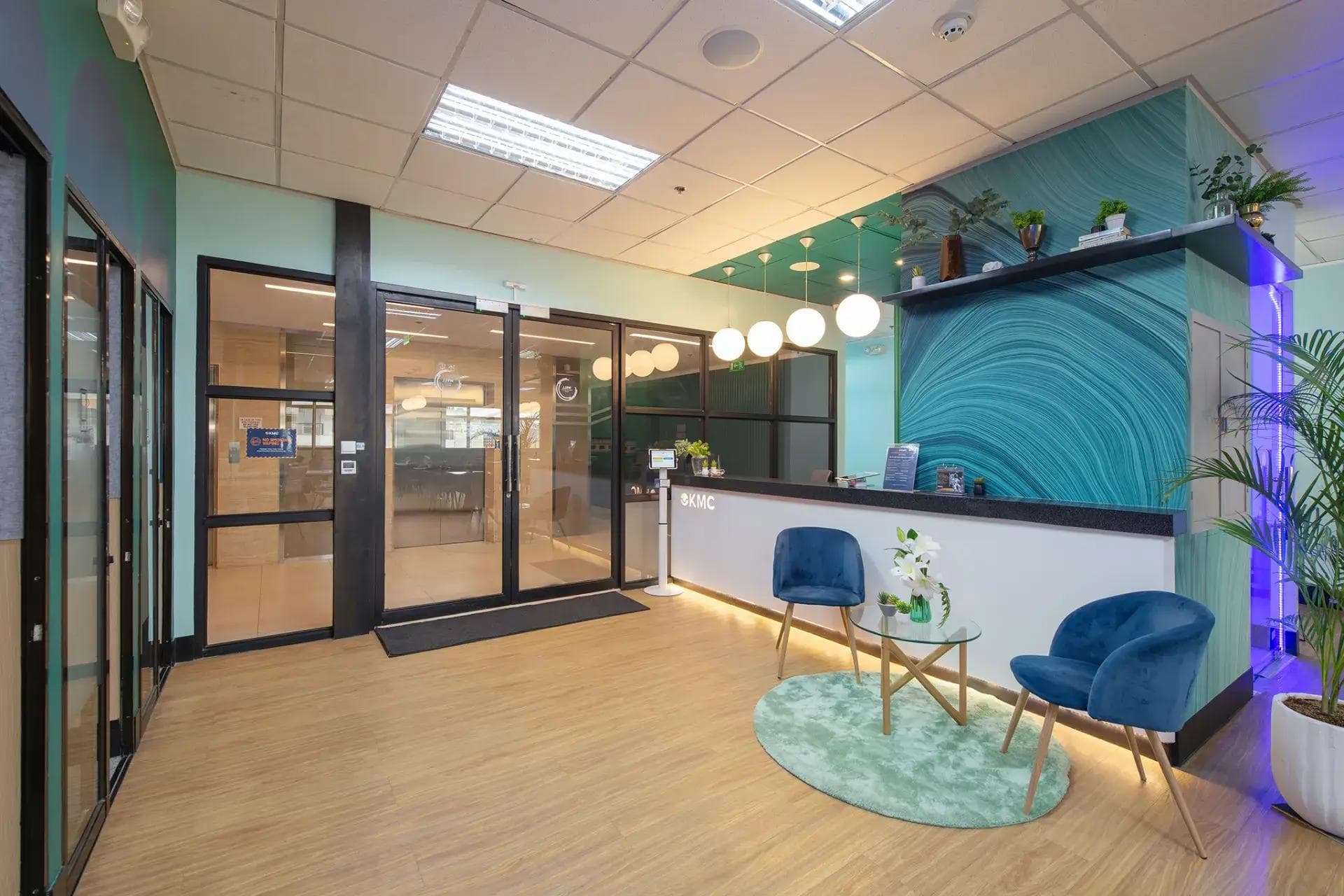 Modern office space in Cebu with teal walls, wood flooring, blue velvet chairs, glass table, and a vibrant reception area.