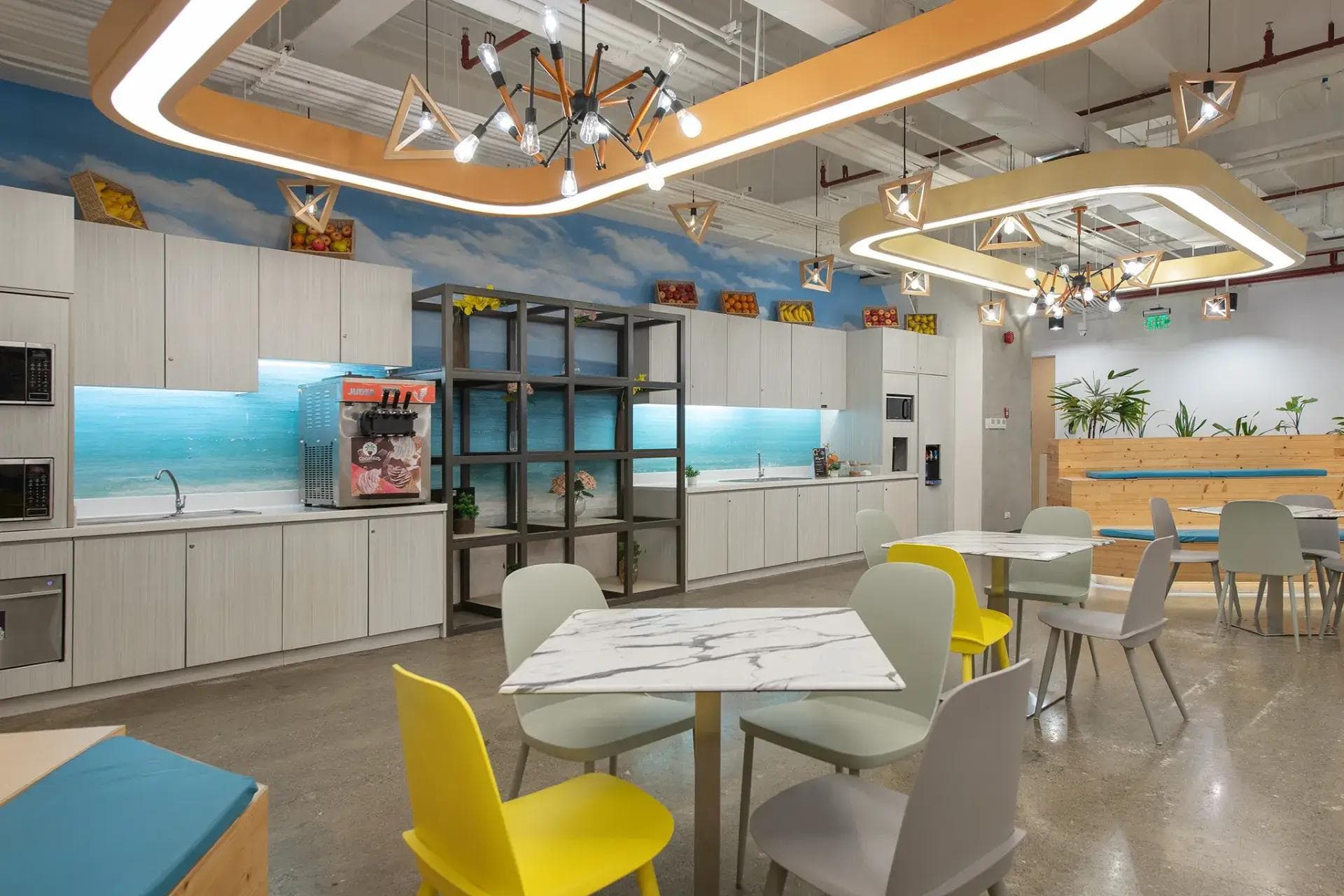 Office space pantry in Skyrise 4B, Cebu with a spacious kitchen, unique lighting, lush decoration and white chairs.