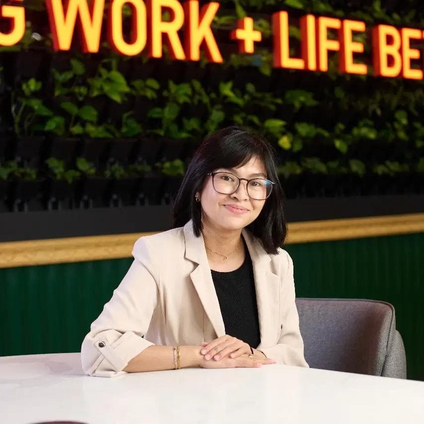 A Filipino content curator seated in a modern and well-lit KMC office space with a “Work + Life Better” sign behind.