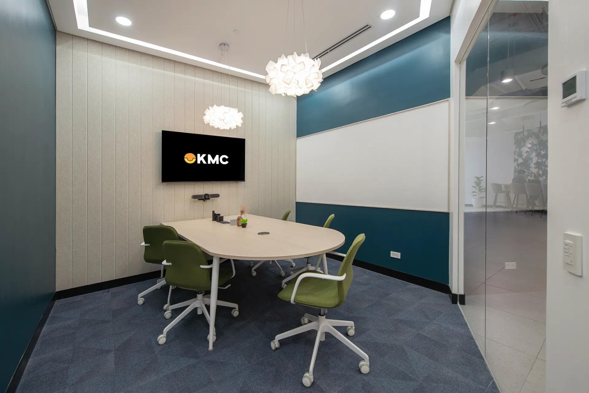 A small meeting room in a private office in One Ayala, Makati with stylish lighting, green chairs, and a wall-mounted TV.
