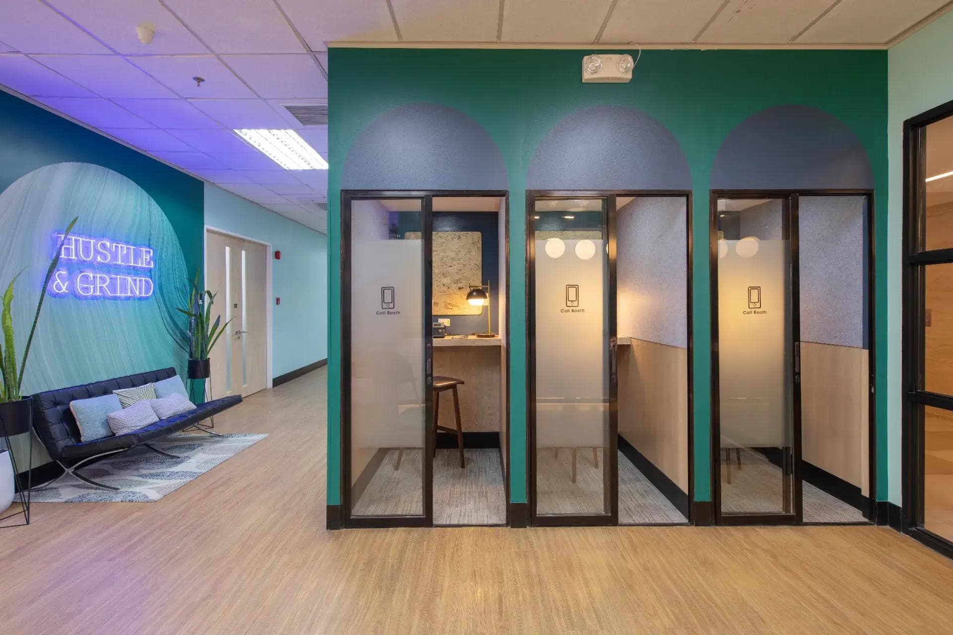 Modern office space in Cebu with teal walls, wood flooring, private call booths, indoor plants, and a neon signage.